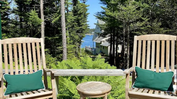 Two deck chairs facing dense pine trees, with only a sliver of water visible beside a neighboring house